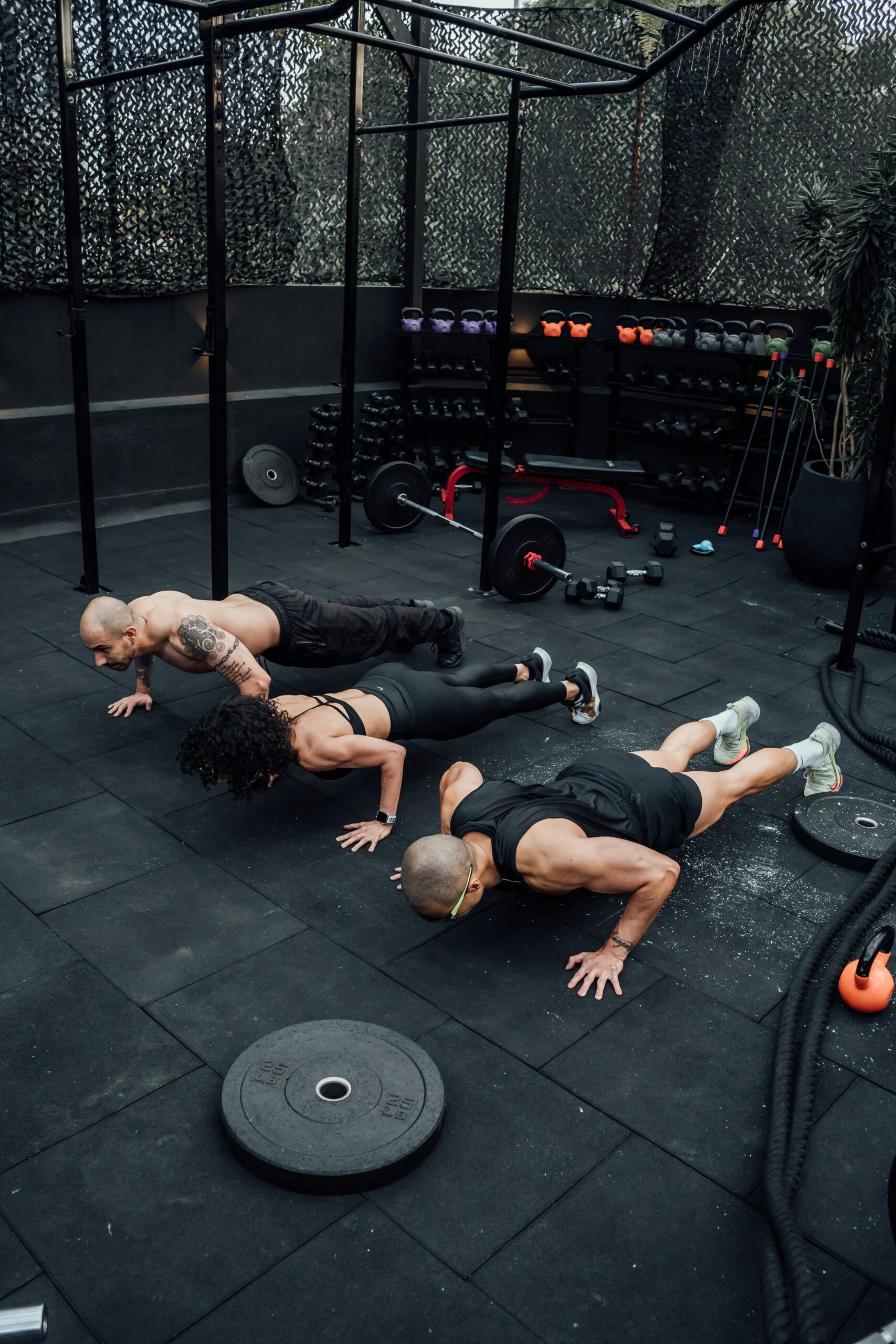 Three adults performing push-ups at an outdoor gym in Mexico City, showcasing strength and teamwork.